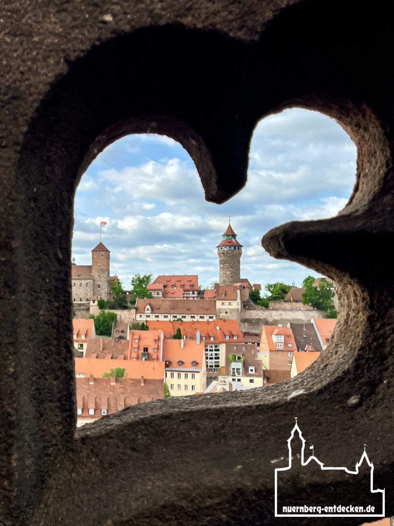 Blick durch die Steinmauer auf dem Nordturm der Sebalduskirche mit Blick auf den Sinwellturm der Kaiserburg.