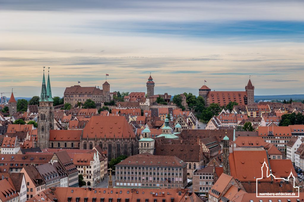 Blick auf das Wahrzeichen von Nürnberg: Im Hintergrund die Kaiserburg mit dem Sinwellturm und Heidenturm. In der Bildmitte die Sebalduskirche mit ihren Zwillingstürmen. Im Vordergrund die Türme des alten Rathauses und der Neubau des wiederaufgebauten Rathauses am Hauptmarkt neben dem Schönen Brunnen. Rechts im Bild die Frauenkirche.